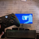 A photo if a hand holding up an Xbox controller in front of a TV